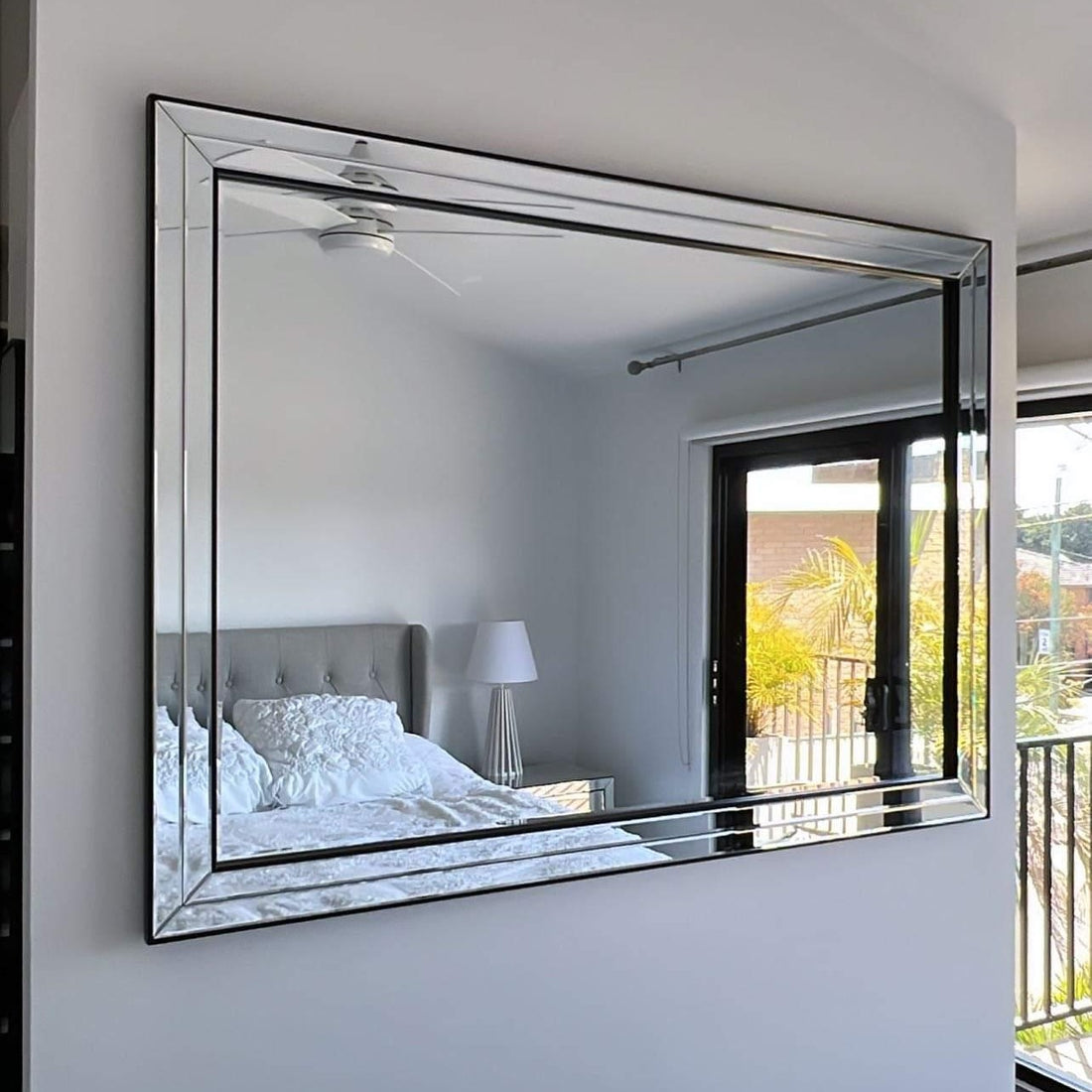 Alma black-framed rectangular wall mirror reflecting a bedroom