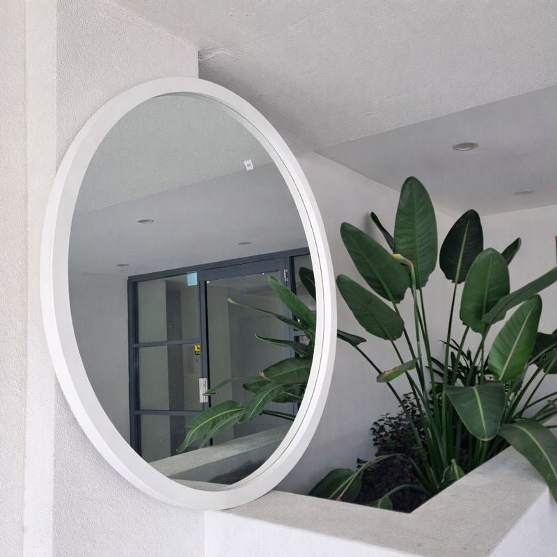 Round white mirror on a wall with plants in the foreground