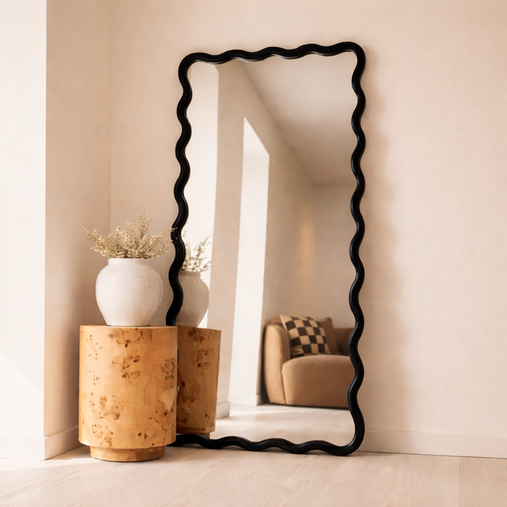 Decorative floor mirror with wavy black frame in a room setting.