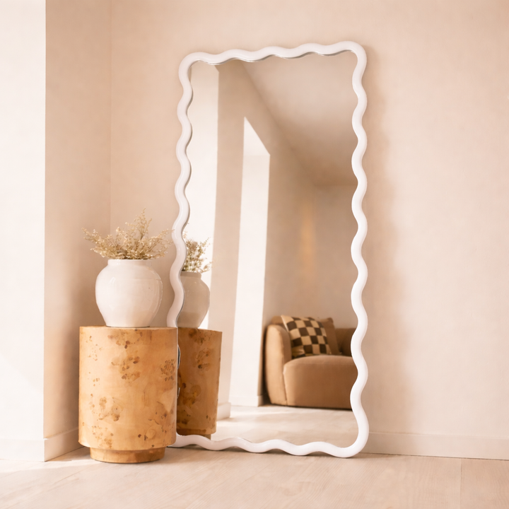 Decorative floor mirror with wavy edge in a room with beige walls and furniture.