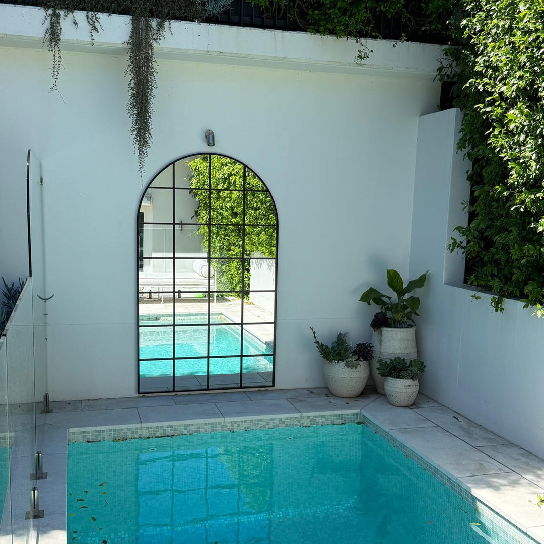 Pool area with white wall, arched window, outdoor mirror, and potted plants