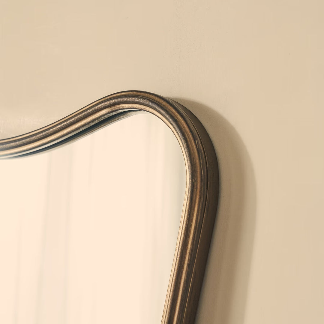 Close-up of a decorative mirror with a wooden frame on a beige wall.