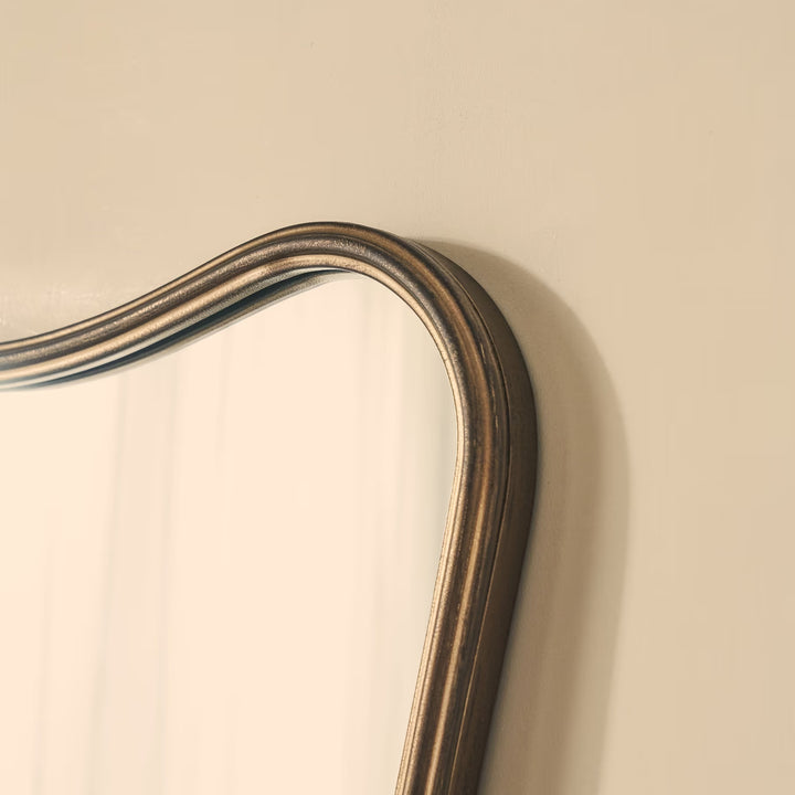 Close-up of a decorative mirror with a wooden frame on a beige wall.