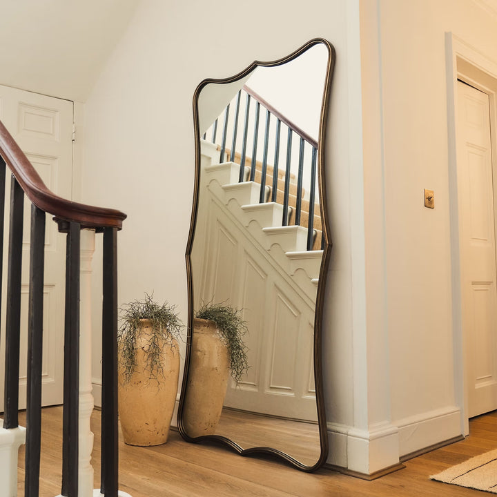 Full-length mirror with decorative frame leaning against a wall in a home setting.