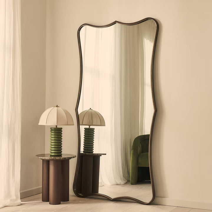 Decorative mirror with wavy frame in a room setting with lamps and curtains.