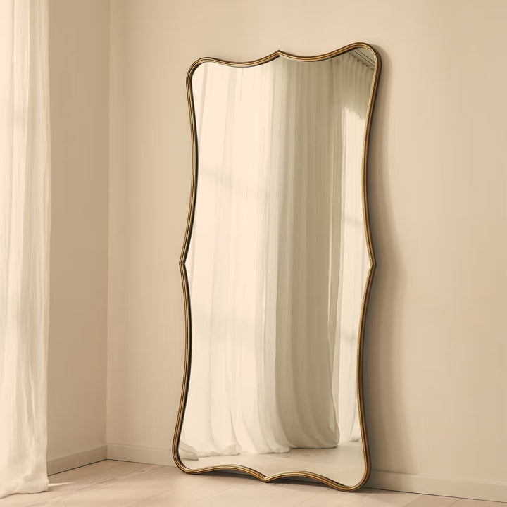 Decorative floor mirror with a gold frame on a beige wall.
