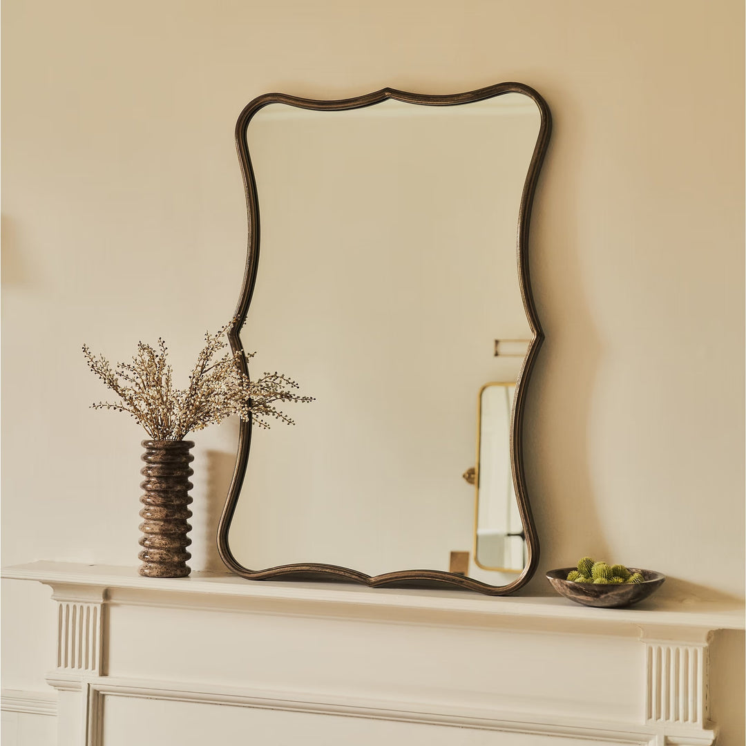 Decorative mirror on a mantelpiece with a vase and bowl.
