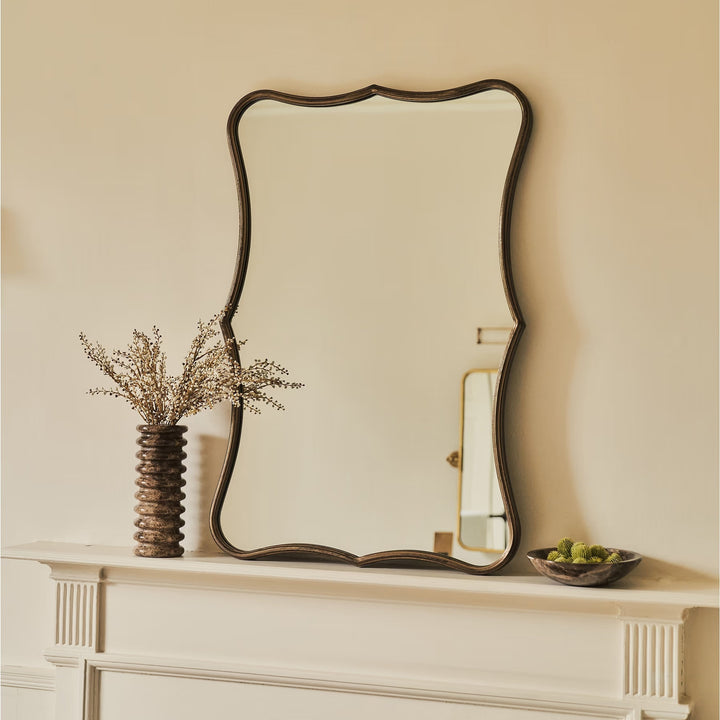 Decorative mirror on a mantelpiece with a vase and bowl.