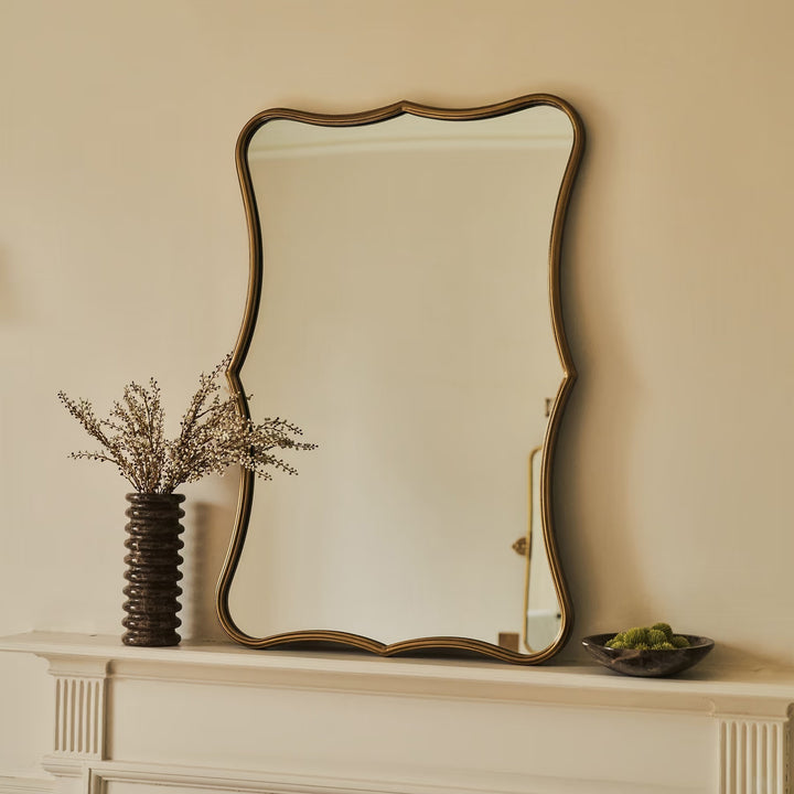 Decorative mirror on a mantelpiece with a vase and small bowl.